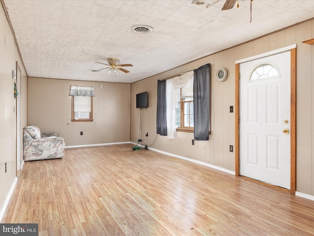 foyer with a wealth of natural light, ceiling fan, wood walls, and light wood-type flooring