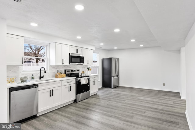 kitchen with white cabinets, sink, decorative backsplash, appliances with stainless steel finishes, and light hardwood / wood-style floors