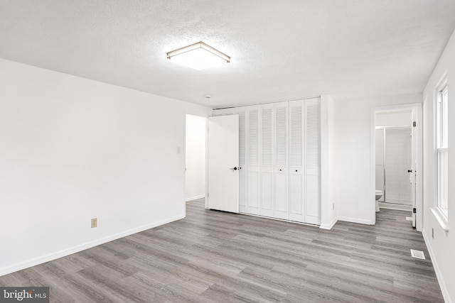 unfurnished bedroom with a textured ceiling, light wood-type flooring, ensuite bathroom, and a closet