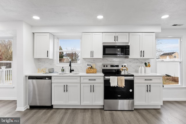 kitchen with appliances with stainless steel finishes, light hardwood / wood-style floors, white cabinetry, and sink