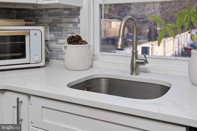 interior details featuring tasteful backsplash, light stone countertops, sink, and white cabinets