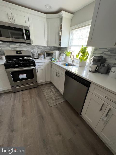 kitchen featuring appliances with stainless steel finishes, dark hardwood / wood-style flooring, sink, and white cabinets