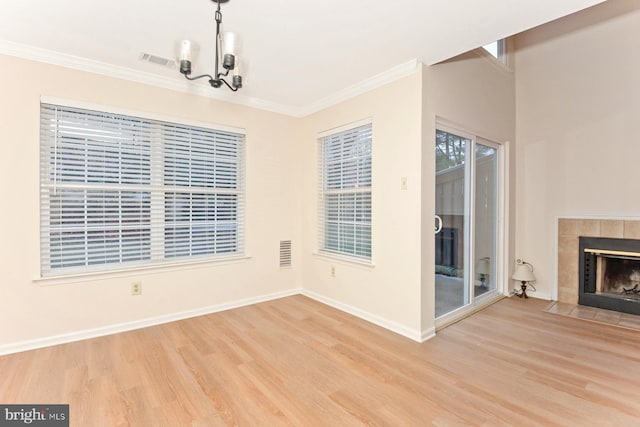 unfurnished dining area with light hardwood / wood-style floors, an inviting chandelier, crown molding, and a tiled fireplace