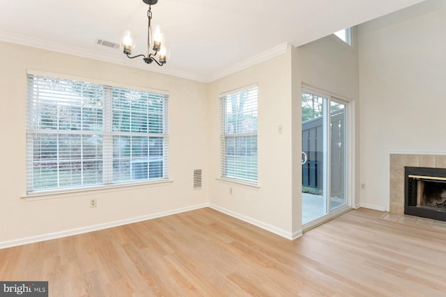 unfurnished dining area with a chandelier, light wood-type flooring, crown molding, and a tiled fireplace