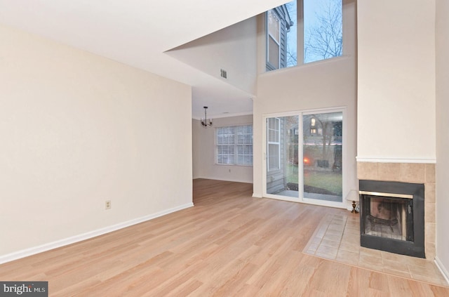 unfurnished living room with a tile fireplace, a towering ceiling, a chandelier, and light wood-type flooring