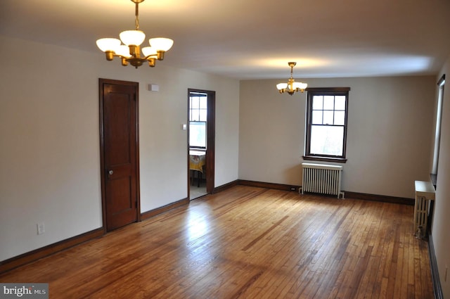 empty room with a chandelier, hardwood / wood-style floors, and radiator