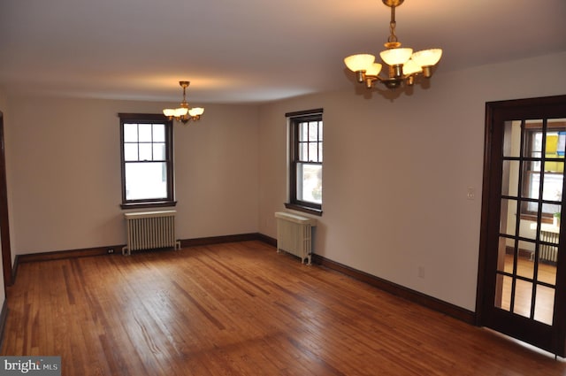 empty room with a notable chandelier, dark hardwood / wood-style flooring, and radiator heating unit