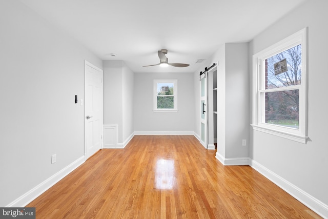 unfurnished room with a barn door, light hardwood / wood-style floors, and ceiling fan