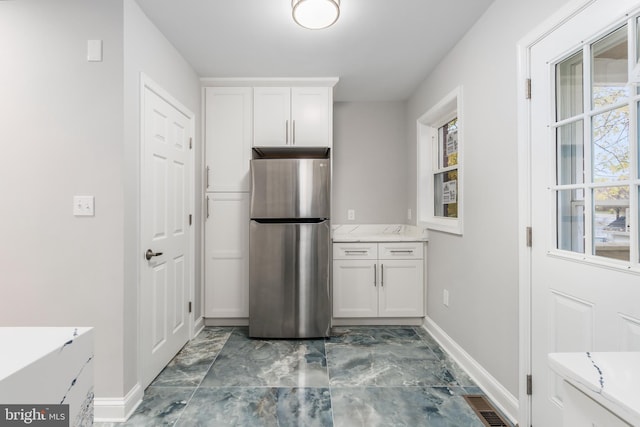 kitchen with white cabinets, stainless steel refrigerator, and light stone counters