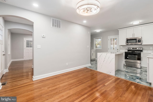 kitchen with white cabinets, light stone counters, stainless steel appliances, and light hardwood / wood-style flooring