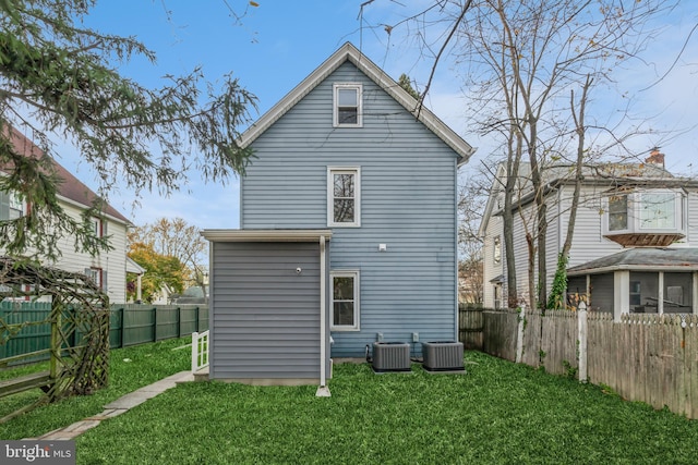 rear view of property featuring central AC unit and a lawn