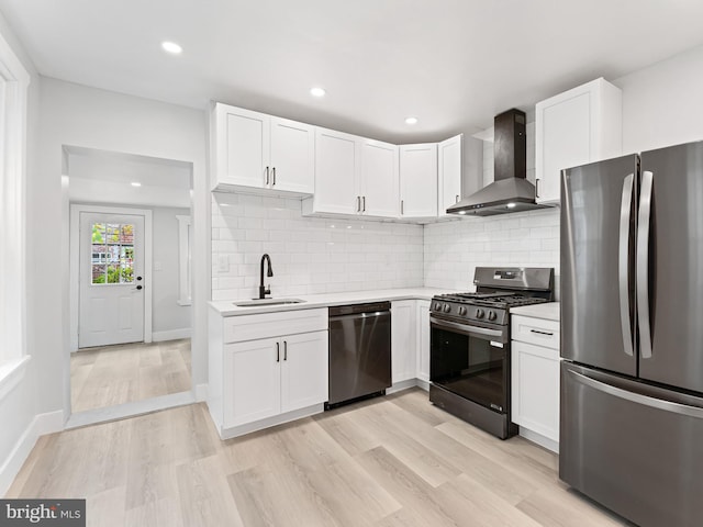 kitchen with black appliances, wall chimney exhaust hood, white cabinets, and sink