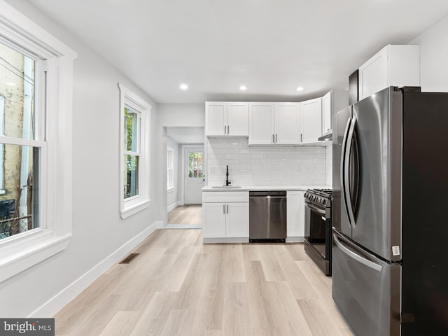 kitchen featuring appliances with stainless steel finishes, light wood-type flooring, white cabinetry, and backsplash