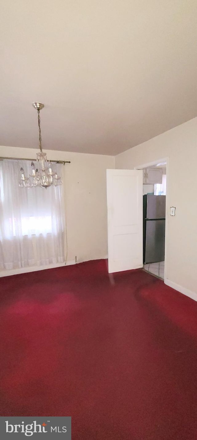 carpeted spare room featuring a notable chandelier