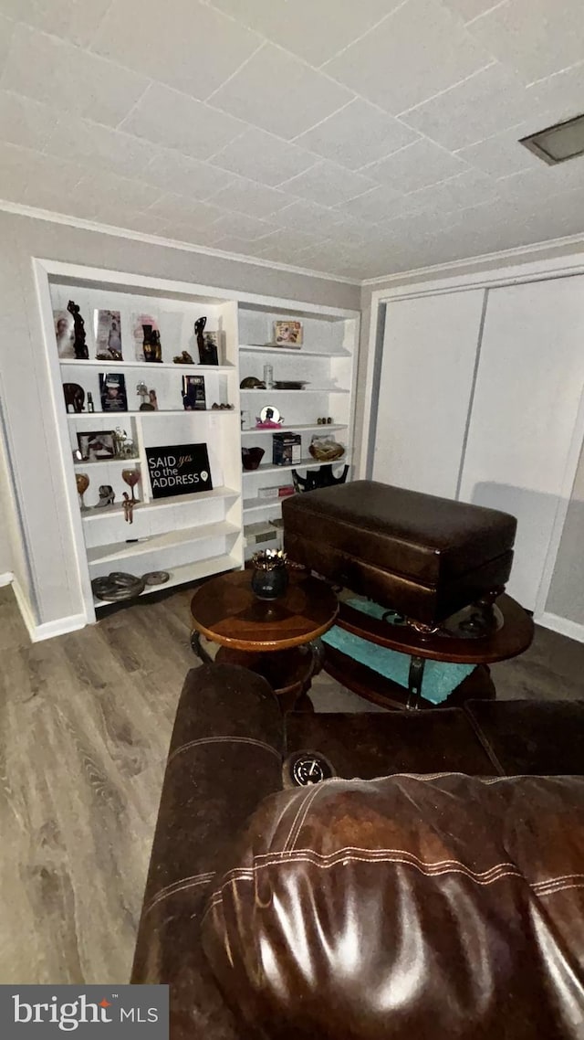 living room featuring wood-type flooring, ornamental molding, and built in shelves