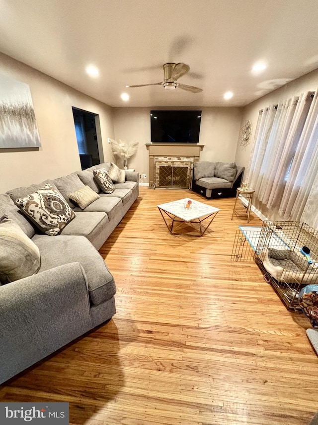 living room featuring a fireplace, light hardwood / wood-style flooring, and ceiling fan