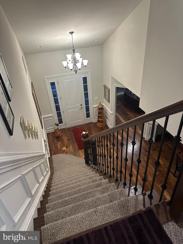 stairs with hardwood / wood-style flooring and an inviting chandelier