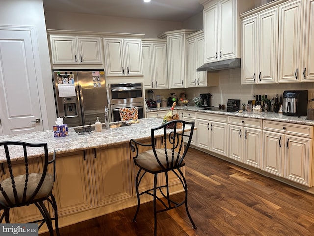 kitchen featuring a breakfast bar area, light stone counters, stainless steel appliances, and dark hardwood / wood-style floors