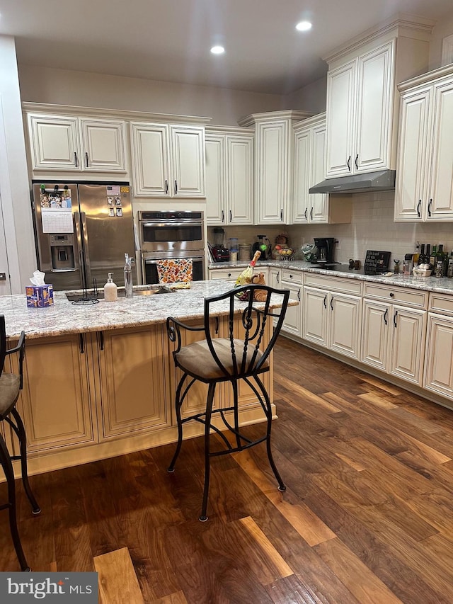 kitchen featuring light stone counters, a breakfast bar, stainless steel appliances, and dark hardwood / wood-style floors