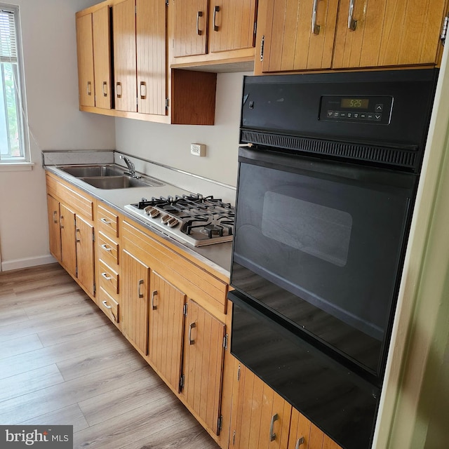 kitchen with stainless steel gas cooktop, sink, black double oven, and light wood-type flooring