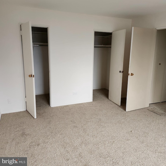 unfurnished bedroom featuring light carpet and multiple closets