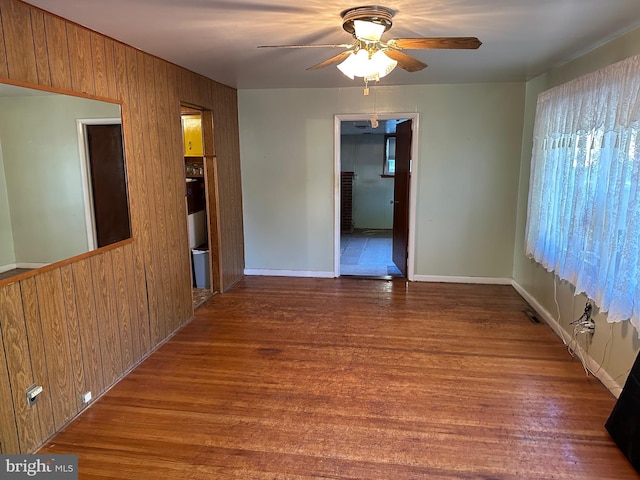 spare room featuring ceiling fan, dark hardwood / wood-style flooring, and wooden walls