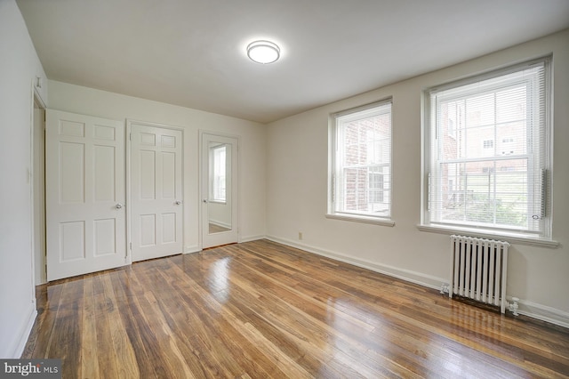 unfurnished bedroom featuring dark hardwood / wood-style floors, radiator, and multiple windows