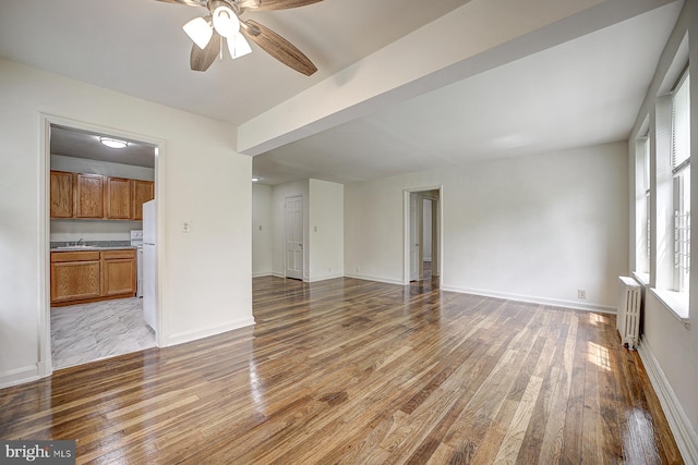 unfurnished living room featuring ceiling fan, sink, wood-type flooring, and radiator heating unit