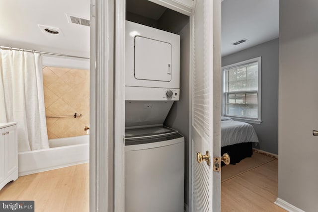 washroom featuring stacked washing maching and dryer and light hardwood / wood-style flooring