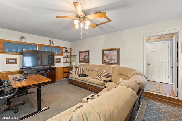 carpeted living room featuring ceiling fan and wood walls