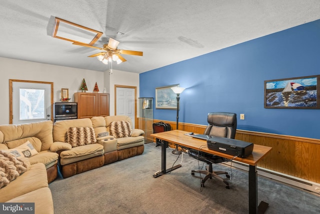 carpeted office space with wood walls, ceiling fan, and a textured ceiling