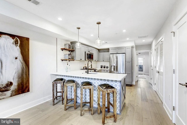 kitchen with gray cabinetry, kitchen peninsula, decorative light fixtures, appliances with stainless steel finishes, and light wood-type flooring