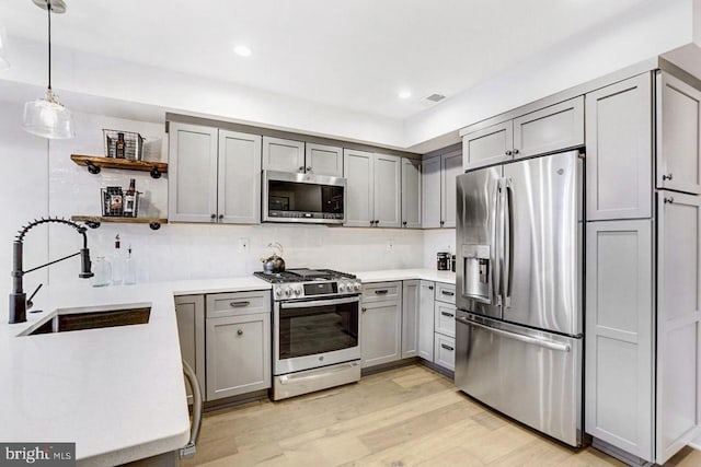 kitchen with appliances with stainless steel finishes, light wood-type flooring, gray cabinetry, sink, and pendant lighting