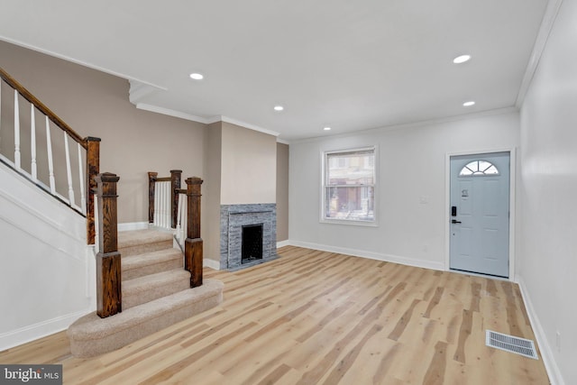 unfurnished living room with a stone fireplace, ornamental molding, and light wood-type flooring