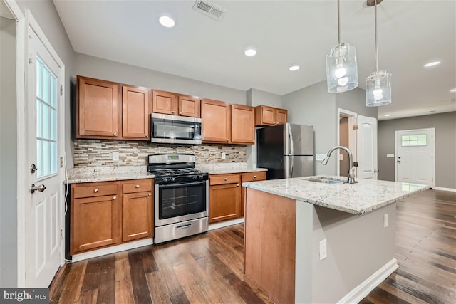 kitchen featuring sink, an island with sink, appliances with stainless steel finishes, dark hardwood / wood-style flooring, and light stone counters