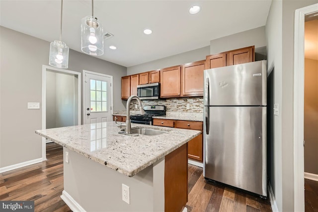 kitchen with dark wood-type flooring, a center island with sink, sink, appliances with stainless steel finishes, and light stone counters