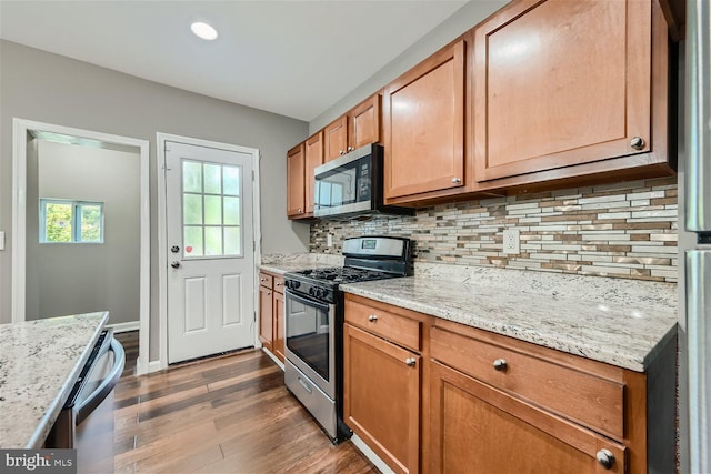 kitchen with decorative backsplash, stainless steel appliances, light stone counters, and dark wood-type flooring