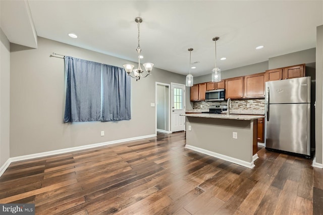 kitchen with hanging light fixtures, light stone counters, dark hardwood / wood-style floors, a kitchen island with sink, and appliances with stainless steel finishes