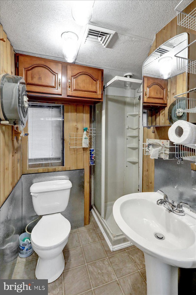 bathroom featuring walk in shower, a textured ceiling, tile patterned flooring, toilet, and wood walls