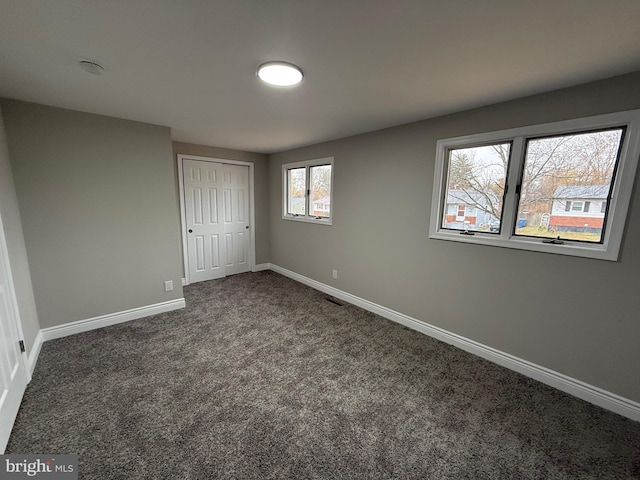 unfurnished bedroom featuring multiple windows, a closet, and dark carpet