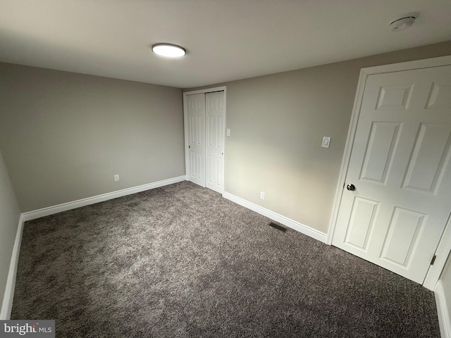 unfurnished bedroom with dark carpet and a closet