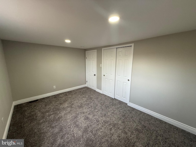 unfurnished bedroom with dark carpet and a closet