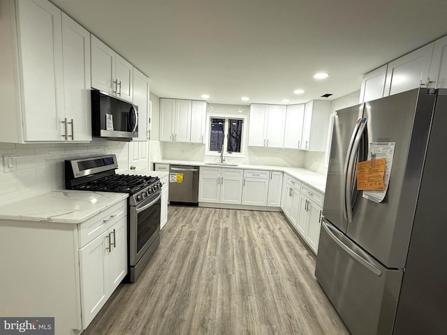 kitchen with white cabinets, sink, decorative backsplash, light hardwood / wood-style floors, and stainless steel appliances