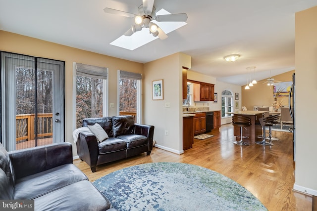 living room with a skylight, ceiling fan, and light hardwood / wood-style floors