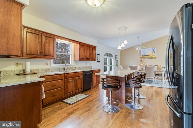 kitchen featuring stainless steel fridge, vaulted ceiling, dishwasher, light hardwood / wood-style floors, and a kitchen island