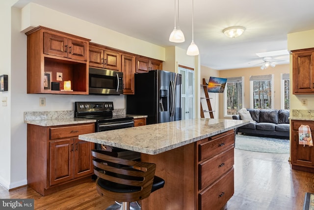 kitchen with dark wood-type flooring, stainless steel appliances, a kitchen breakfast bar, light stone counters, and decorative light fixtures