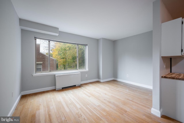 spare room featuring light wood-type flooring and radiator