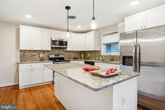 kitchen featuring white cabinetry, sink, hanging light fixtures, stainless steel appliances, and a kitchen island