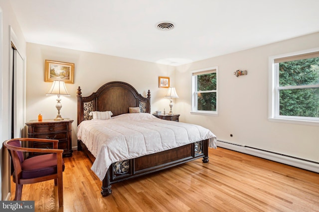 bedroom featuring a baseboard heating unit, light wood-type flooring, and multiple windows