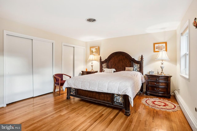 bedroom featuring light wood-type flooring, two closets, and a baseboard radiator